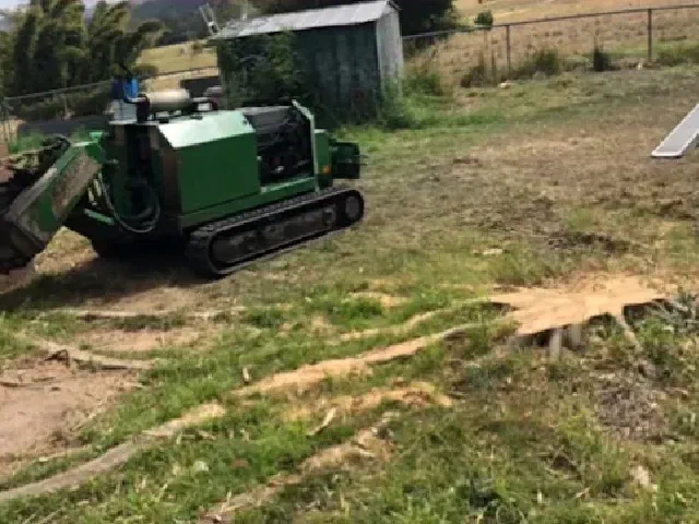 Stump grinder beside a house with a freshly cut stump in the lawn