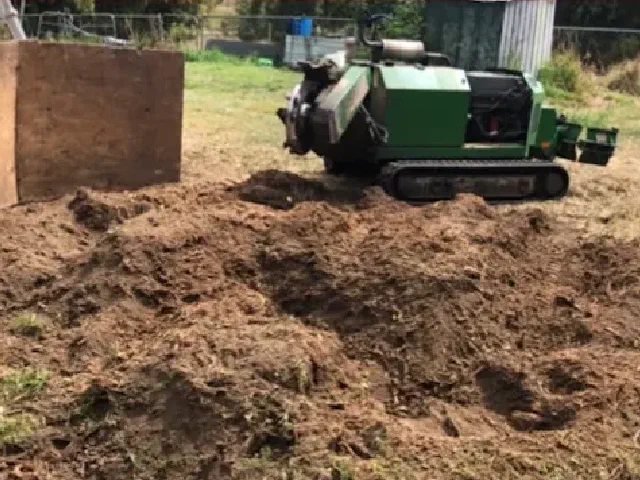 Mound of stump grindings with a guard board and the grinder behind it